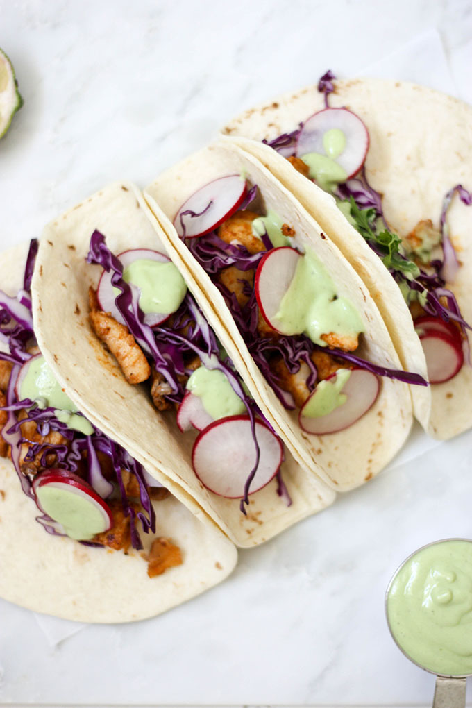 healthy fish tacos on marble board with cabbage, radish and a avocado dressing