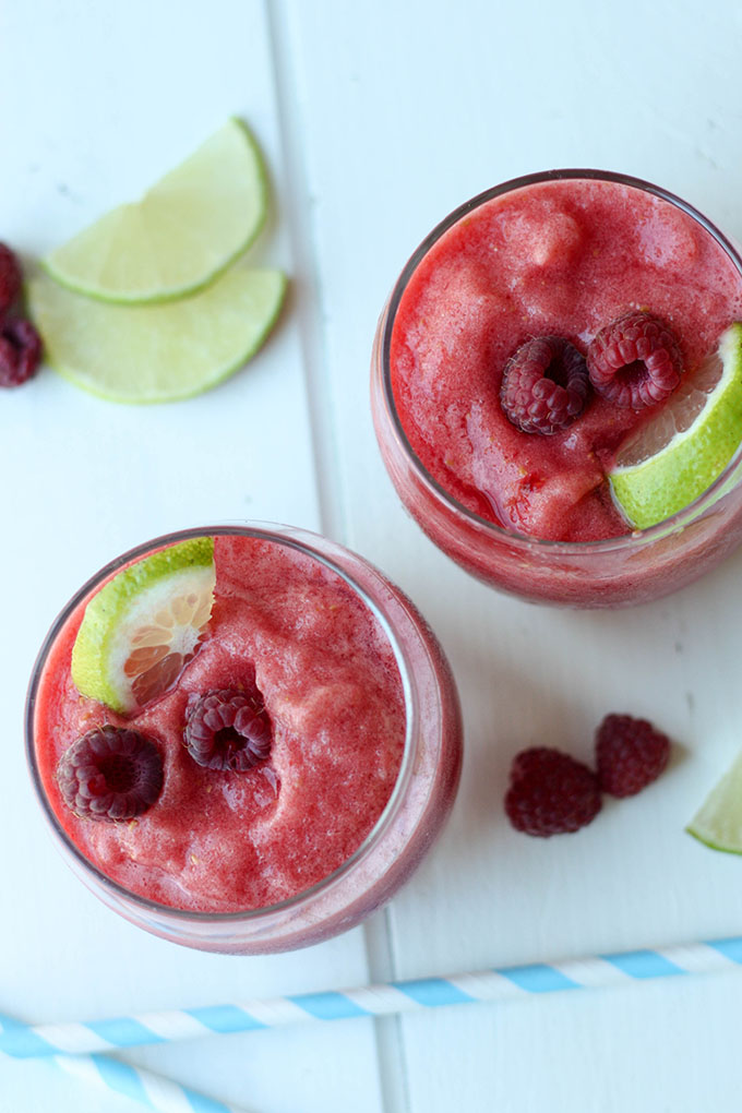 Two raspberry margaritas in small glasses, garnished with fresh lime and raspberries