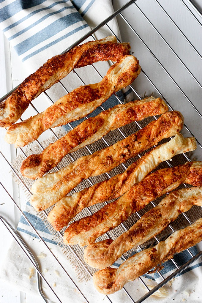 overhead parmesan puff pastry cheese straws on a wire rack, above blue and white tea towel