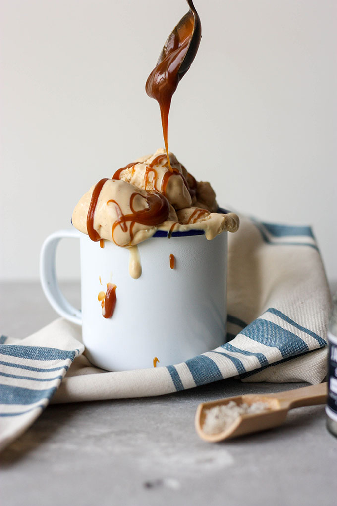 spoon drizzling caramel over a cup of no churn ice cream on a blue and white napkin