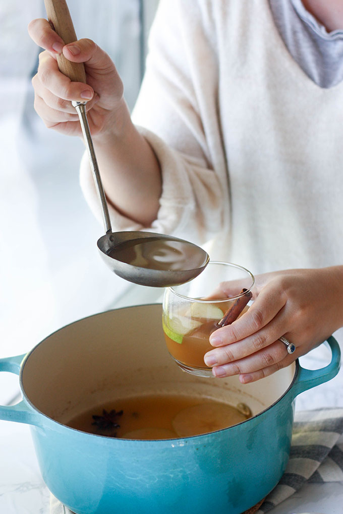 person ladling hot spiced apple cider into glass