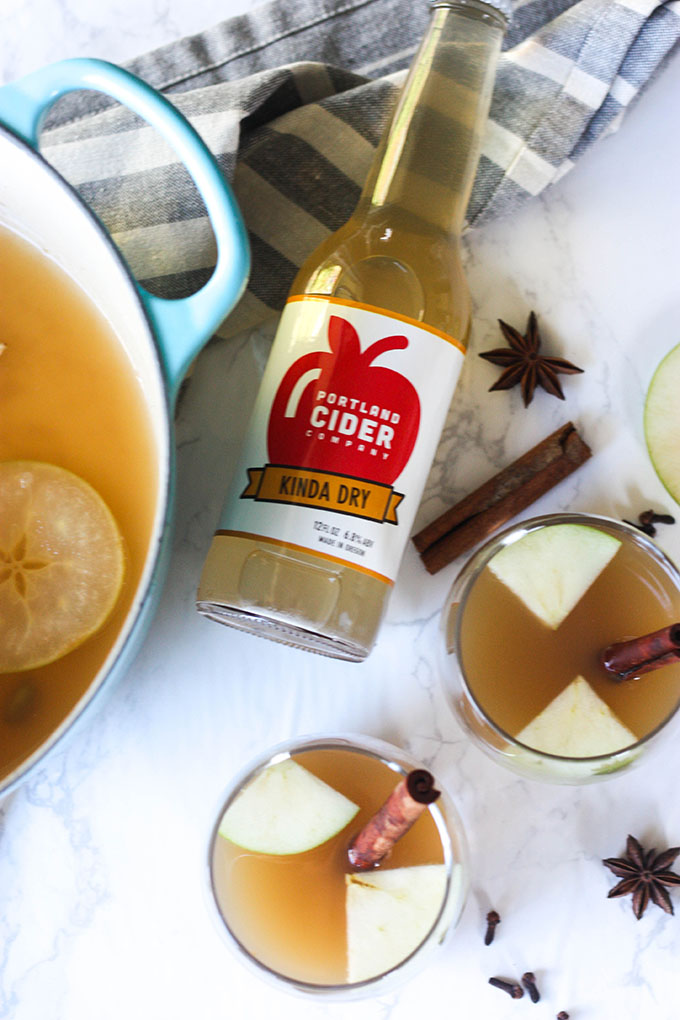 hot spiced apple cider in glasses on marble board, cider bottle and dutch oven in image 