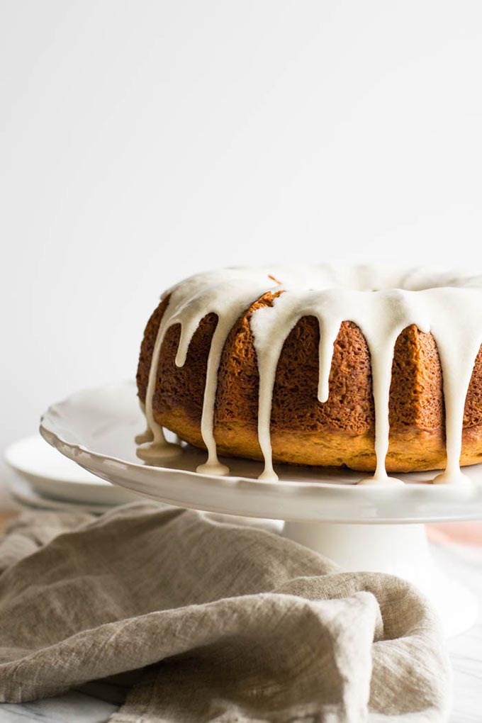pumpkin spiced bundt cake on white cake stand with brown linen