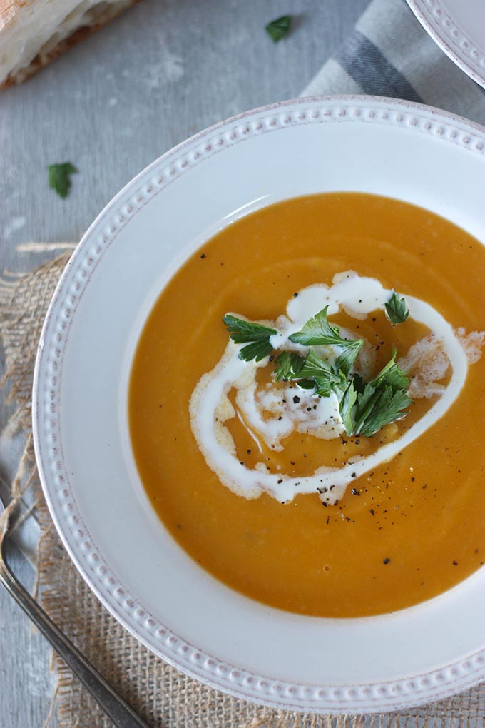 white bowl of pumpkin sweet potato soup with cream and parsley garnish