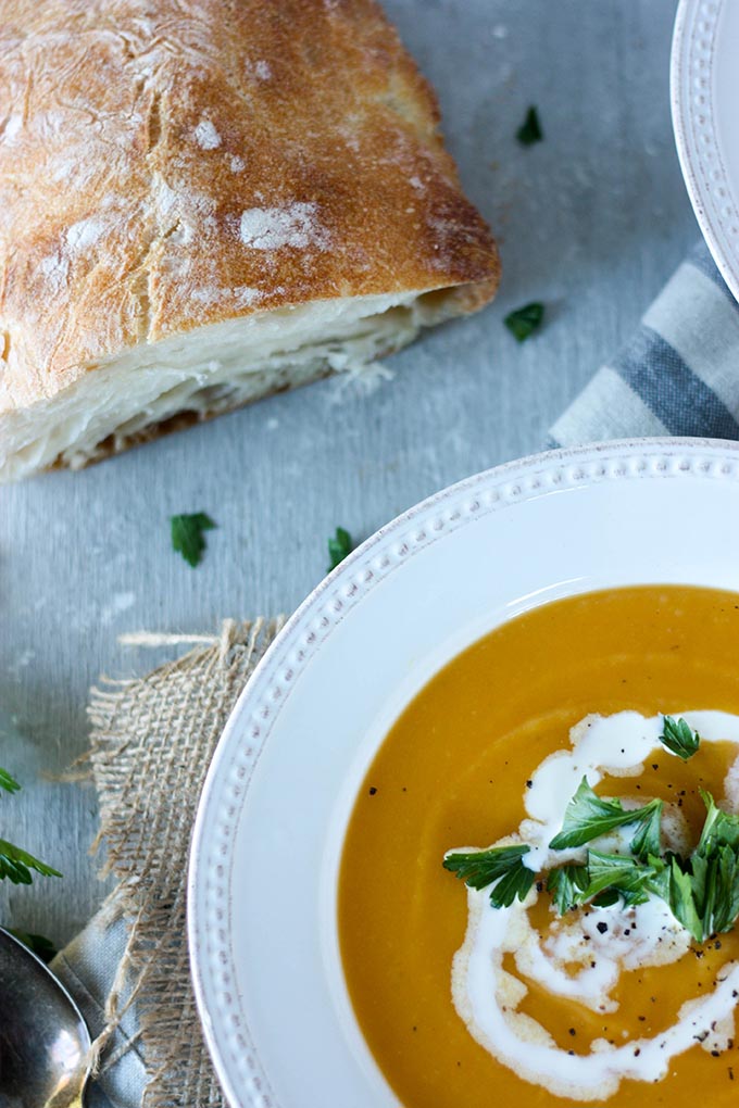 bowl of pumpkin sweet potato soup next to crusty loaf of bread