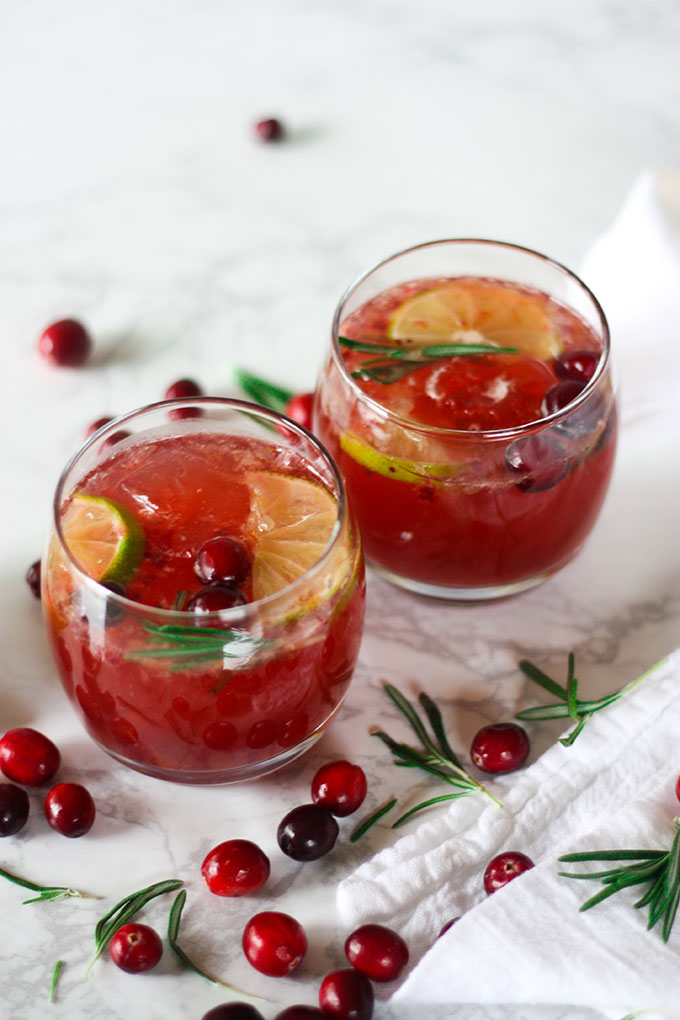 two glasses of cranberry rosemary bourbon punch on white marble board