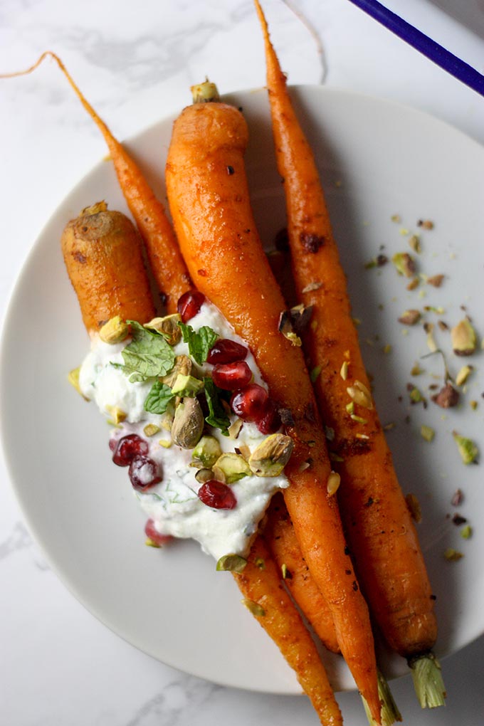 four harissa roasted carrots on a small white plate, topped with mint lemon yogurt and garnish