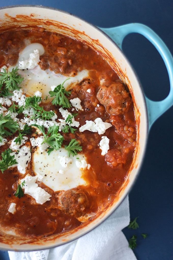 blue dutch oven, close up of spicy shakshuka garnished with parsley and goat cheese