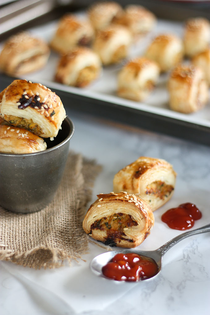 close up of thai chicken sausage rolls in antique cup, teaspoon of tomato ketchup next to sausage rolls on board