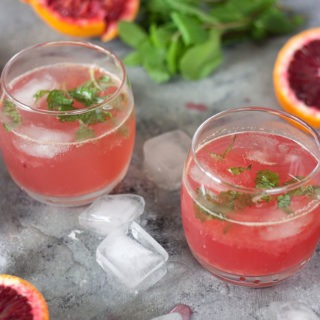 two blood orange cocktails on a grey board with cut winter citrus