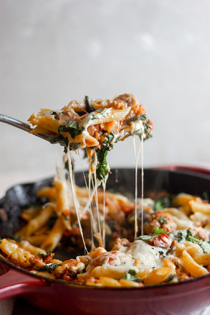 a spoonful of pasta being lifted from a skillet leaving a string of cheese