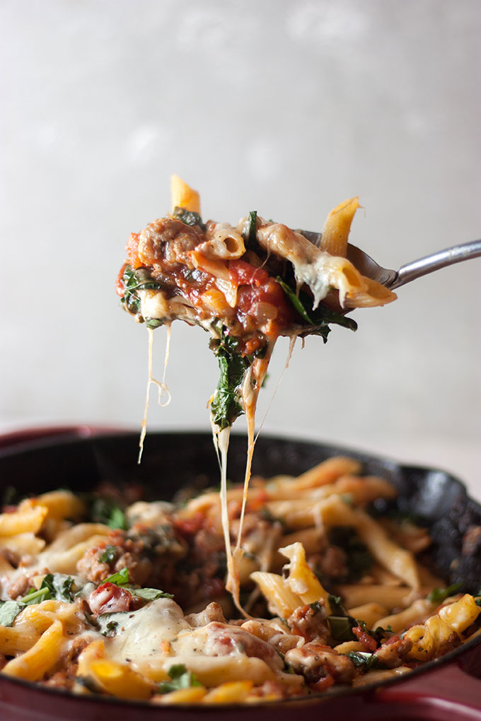 a spoonful of cheesy pasta lifted from a skillet pan