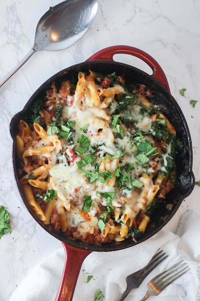 a red skillet with baked pasta, italian sausage and melted cheese