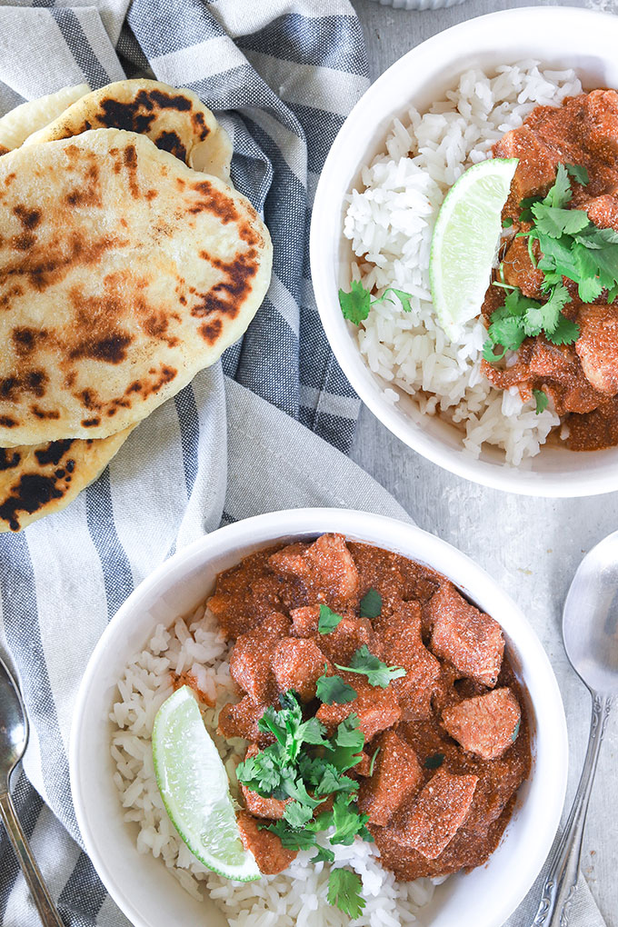 two bowls of chicken yogurt curry on a napkin with rice and naan