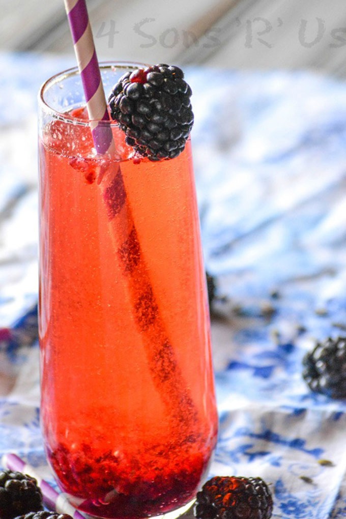 tall glass of blackberry champagne cocktails with straw and blackberry garnish