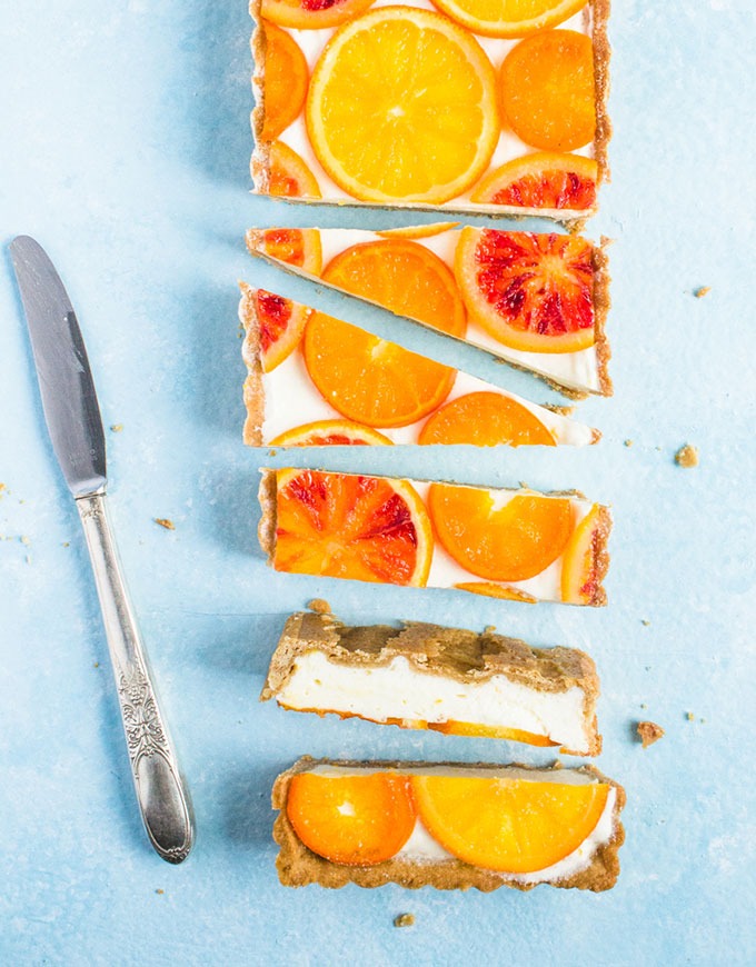 bright mimosa citrus tart cut into pieces on blue background with vintage butter knife on left