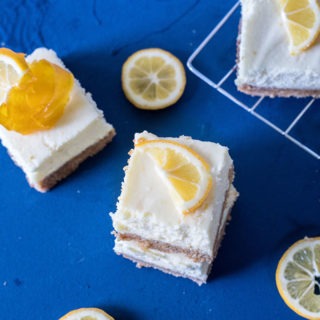three pieces of lemon cheesecake bars on a board, three pieces of lemon slices and wire rack