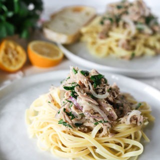 white plate piled with tuna lemon pasta, second plate in background next to lemon wedges and parsley
