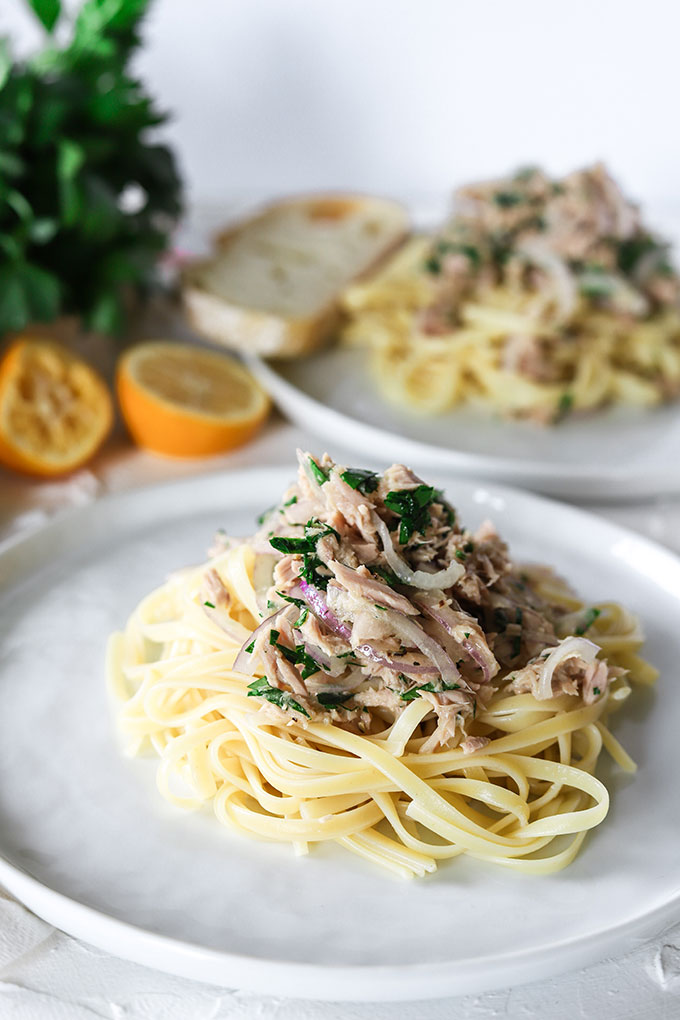 white plate piled with tuna lemon pasta, second plate in background next to lemon wedges and parsley