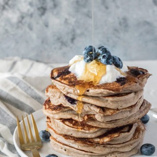 stack of kefir pancakes on a white plate with gold fork