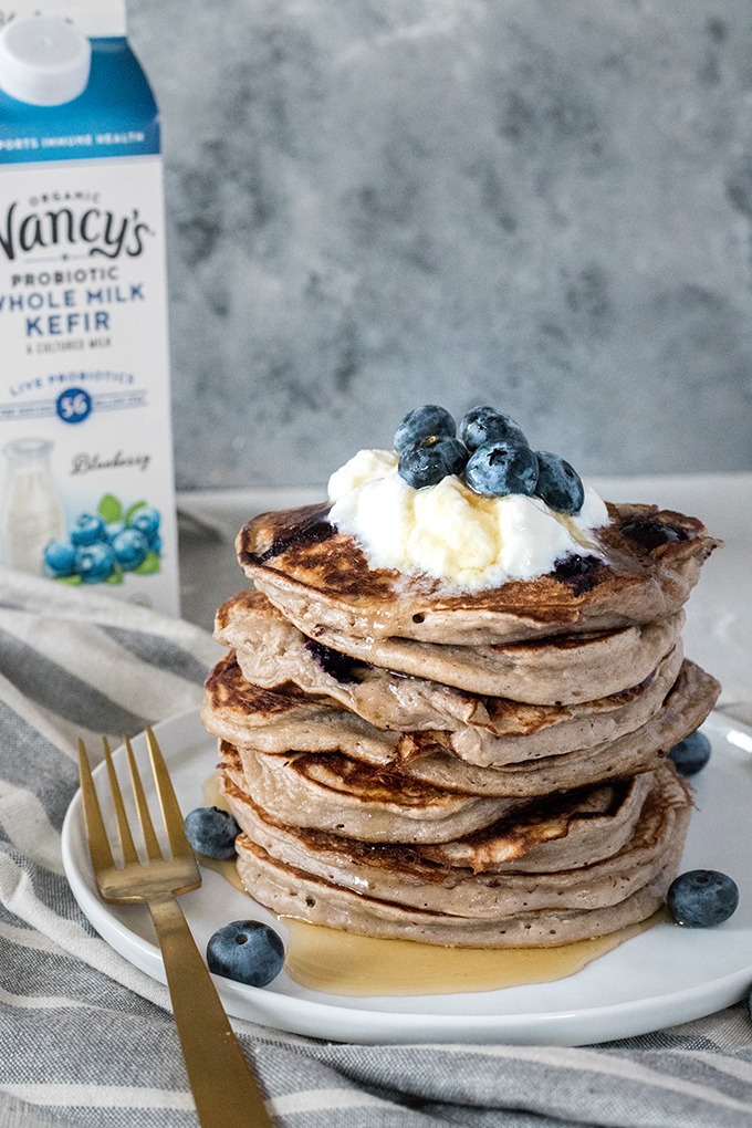 stack of kefir pancakes on white plate in front of carton of blueberry kefir