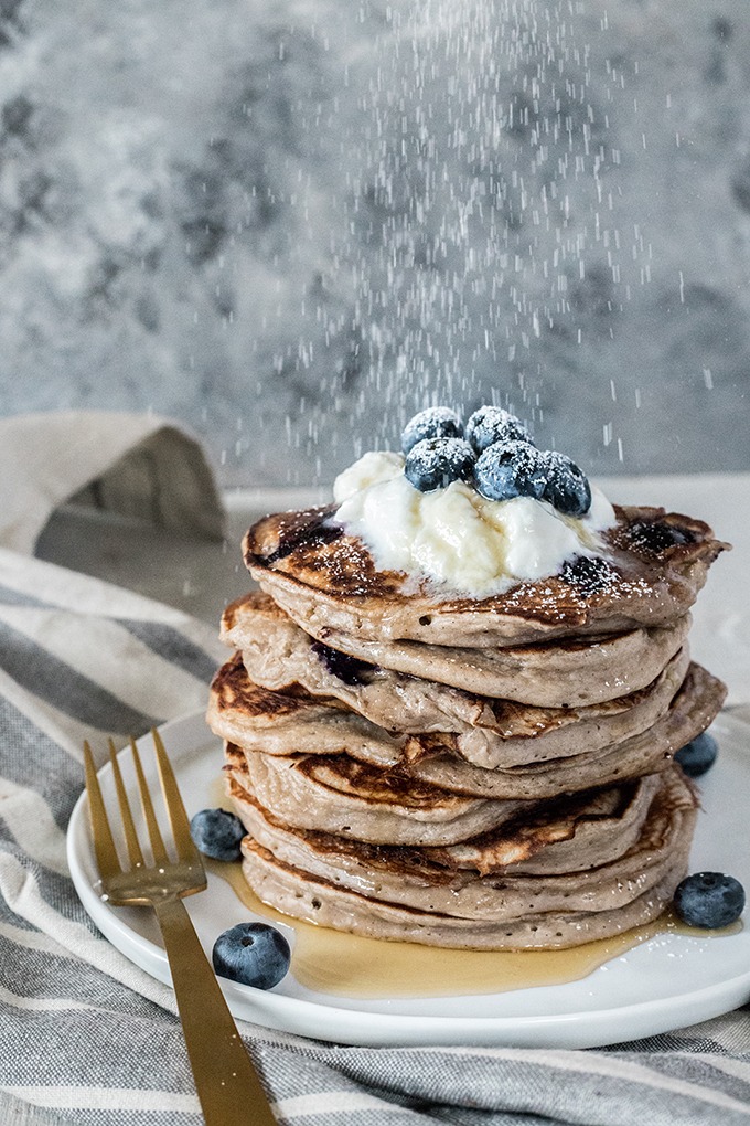 powdered sugar being sprinkled on top of blueberry pancakes