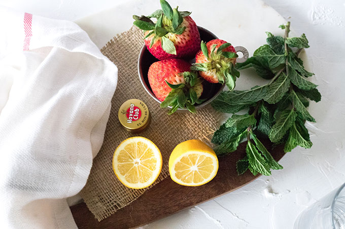 marble wooden board, two lemons, one cup of strawberries and mint leaves