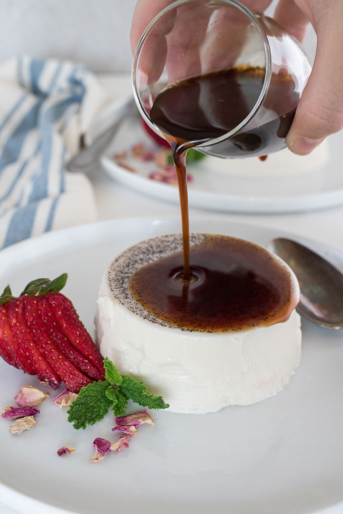 espresso syrup being poured over a vanilla panna cotta on white plate