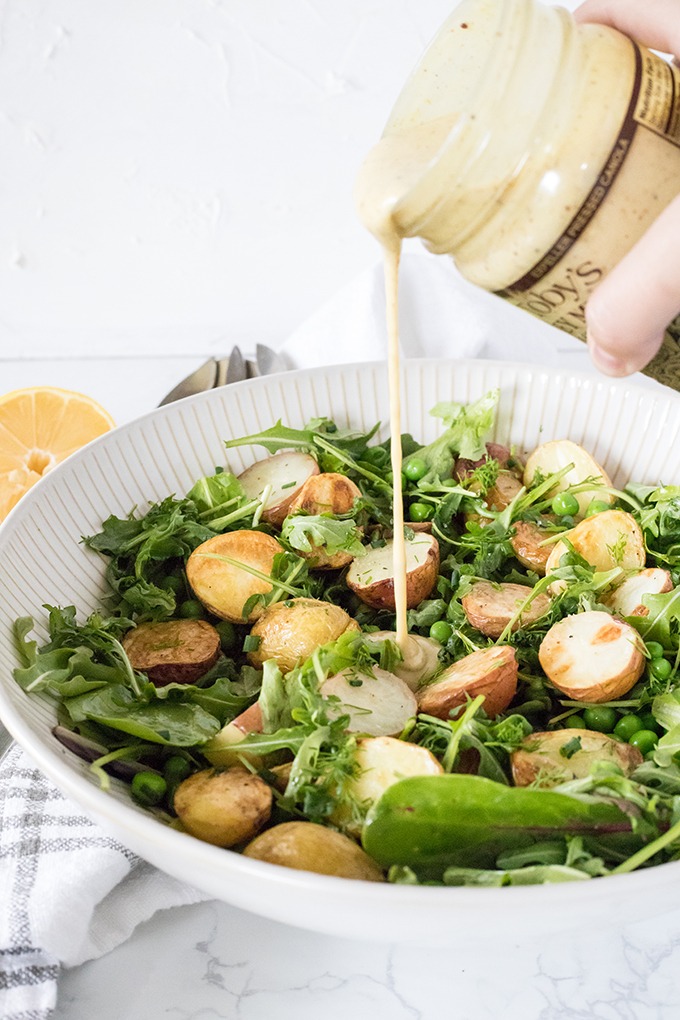 honey mustard dressing being poured over potato salad in white bowl