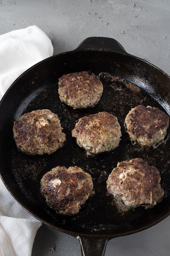 lamb burgers with feta cooking on cast iron, lightly browned and charred