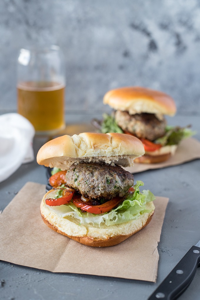 two lamb burgers with feta on brown parchment paper, in front of glass of beer