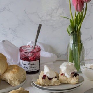 plate of lemonade scones with jam and cream in front of vase of tulips and jam jar