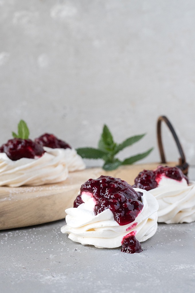 one vanilla meringue topped with blackberry sauce on a grey board, round antique board with other meringues in background
