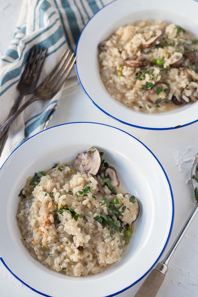 two plates of mushroom and pea risotto on a white backdrop