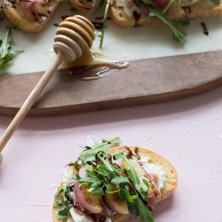 one piece of bruschetta with proscuitto nectarine and arugula on pink board in front of marble board