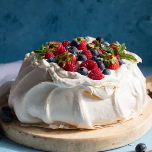 pavlova topped with cream and berries on an antique round wooden board