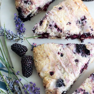 three blackberry scones on a marble board with fresh lavender and blackberries