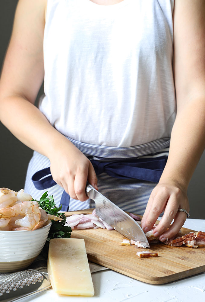 person standing behind a table cutting bacon on a wooden board