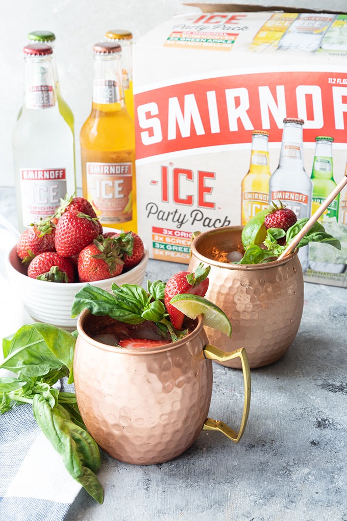 two strawberry basil mule mugs in front of Smirnoff ice party pack, and four bottles of Smirnoff ice 