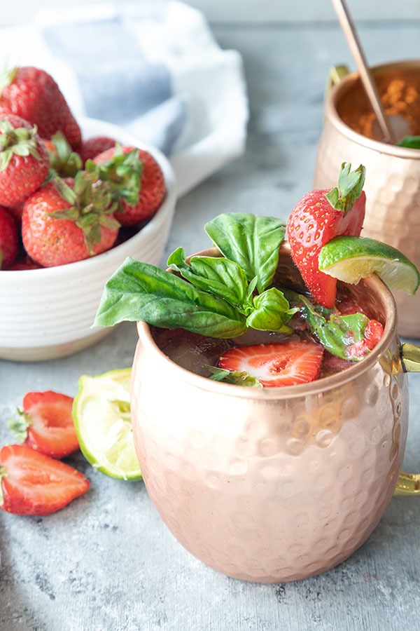 strawberry basil mule in copper mug, bowl of strawberries and white linen in background