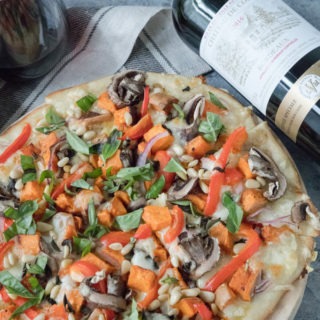veggie pizza on wooden board with bottle of wine