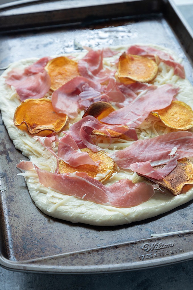 prosciutto and butternut squash on raw pizza base on baking tray
