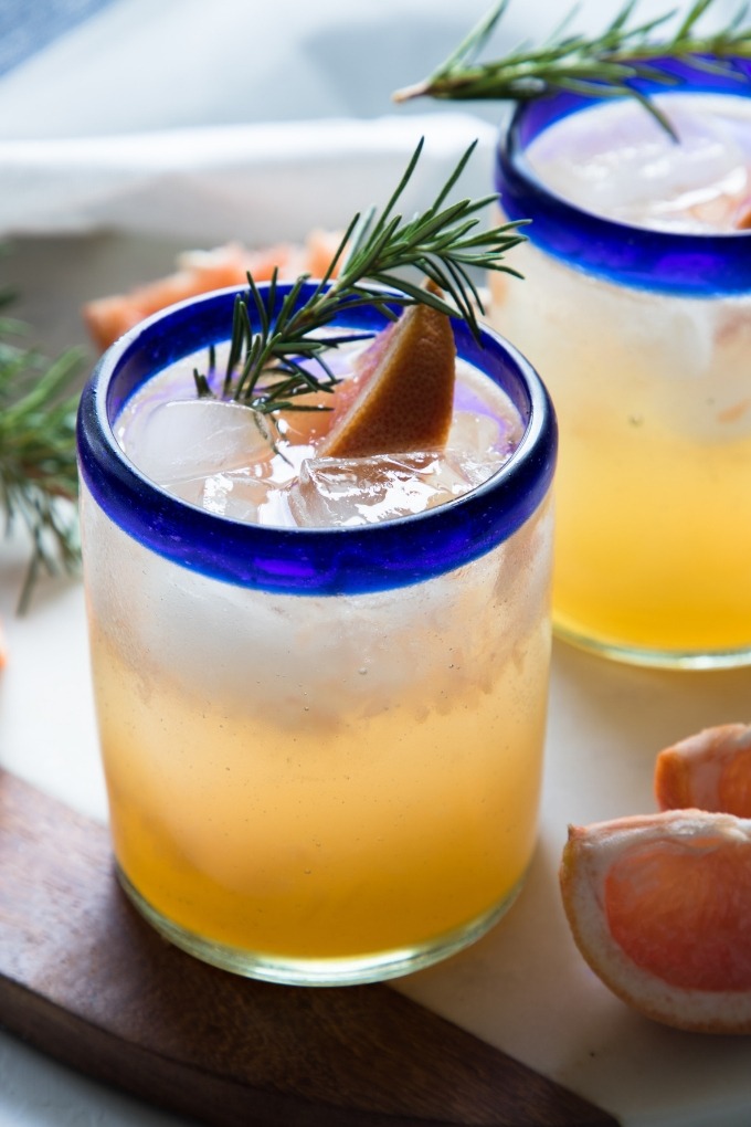 grapefruit gin cocktail in clear glass with blue rim garnished with rosemary and grapefruit