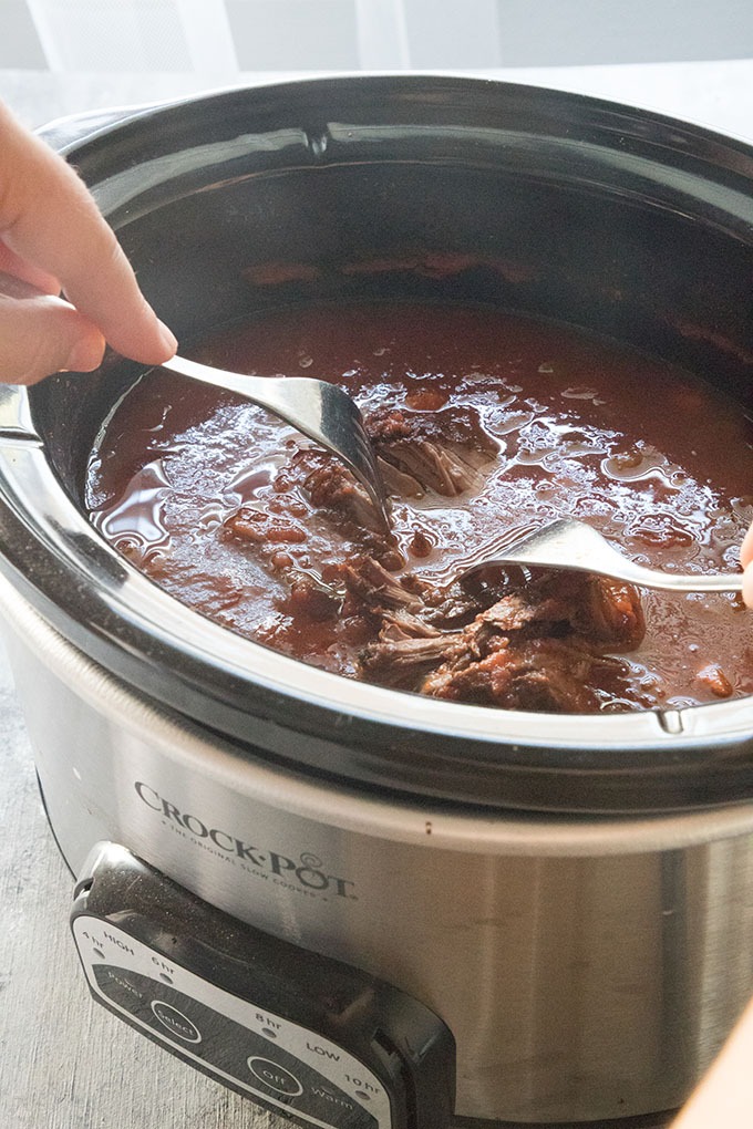 hand holding two forks shredding beef in slow cooker