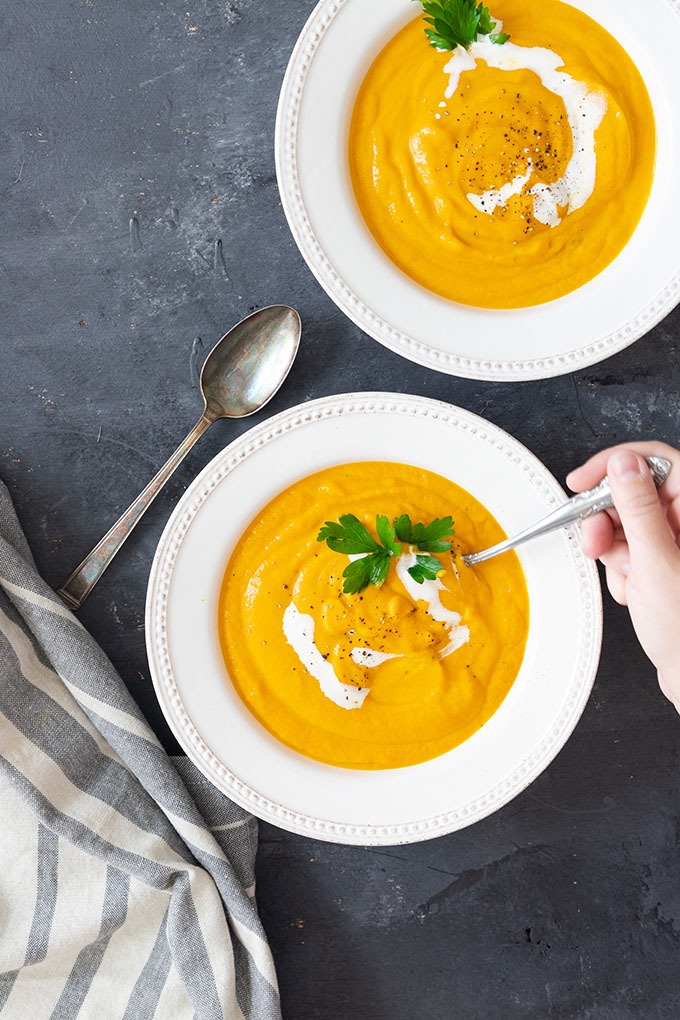hand reaching out with a spoon to dip into carrot ginger soup