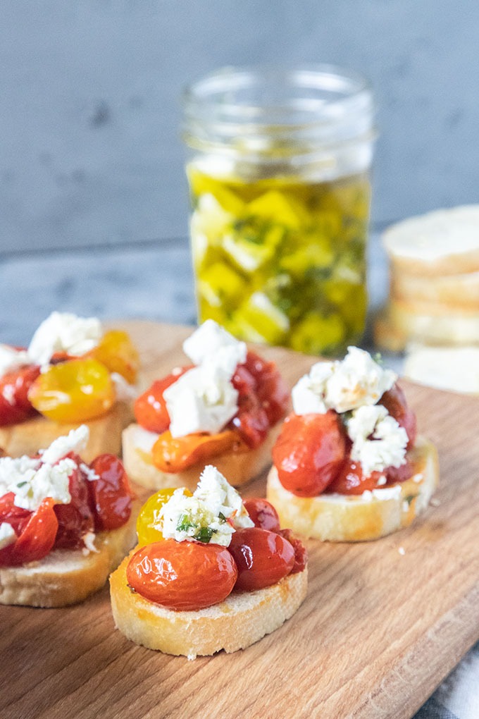tomato crostini on wooden board in front of marinated feta 