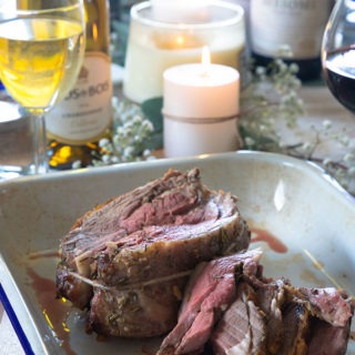 boneless lamb roast on table with Wine and sides in background