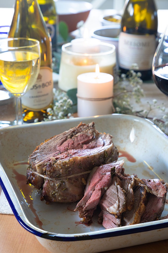 boneless lamb roast on table with Wine and sides in background