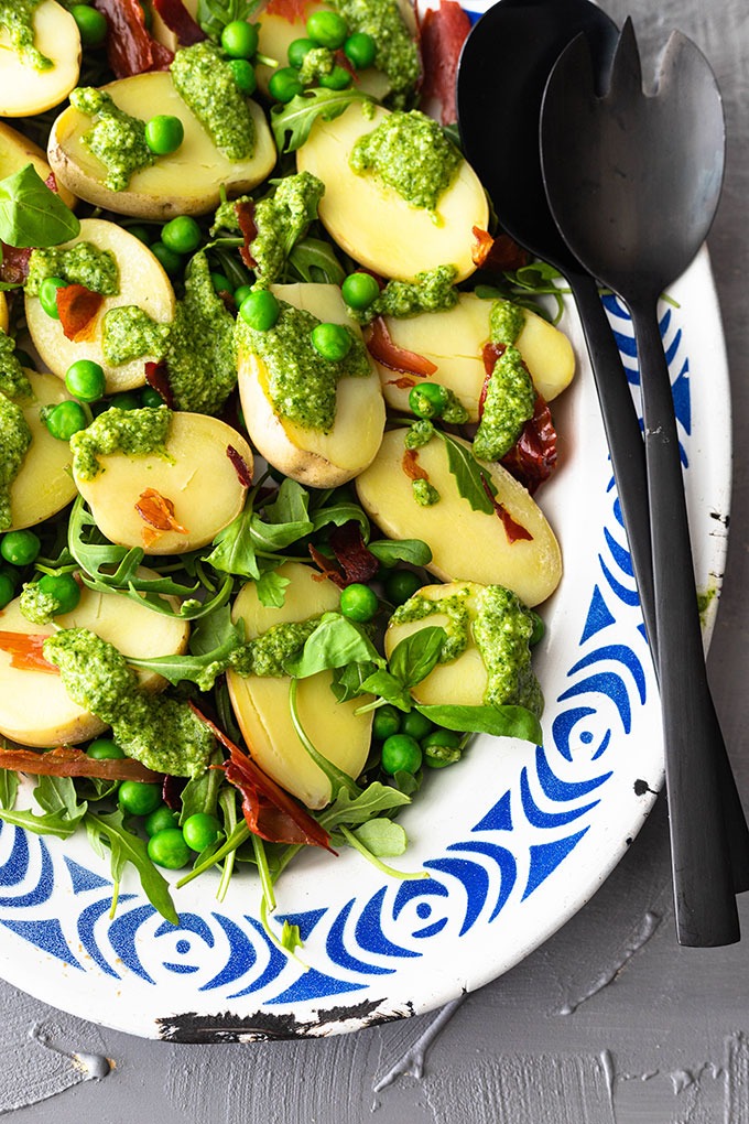 pesto potato salad on blue and white plate with black salad servers