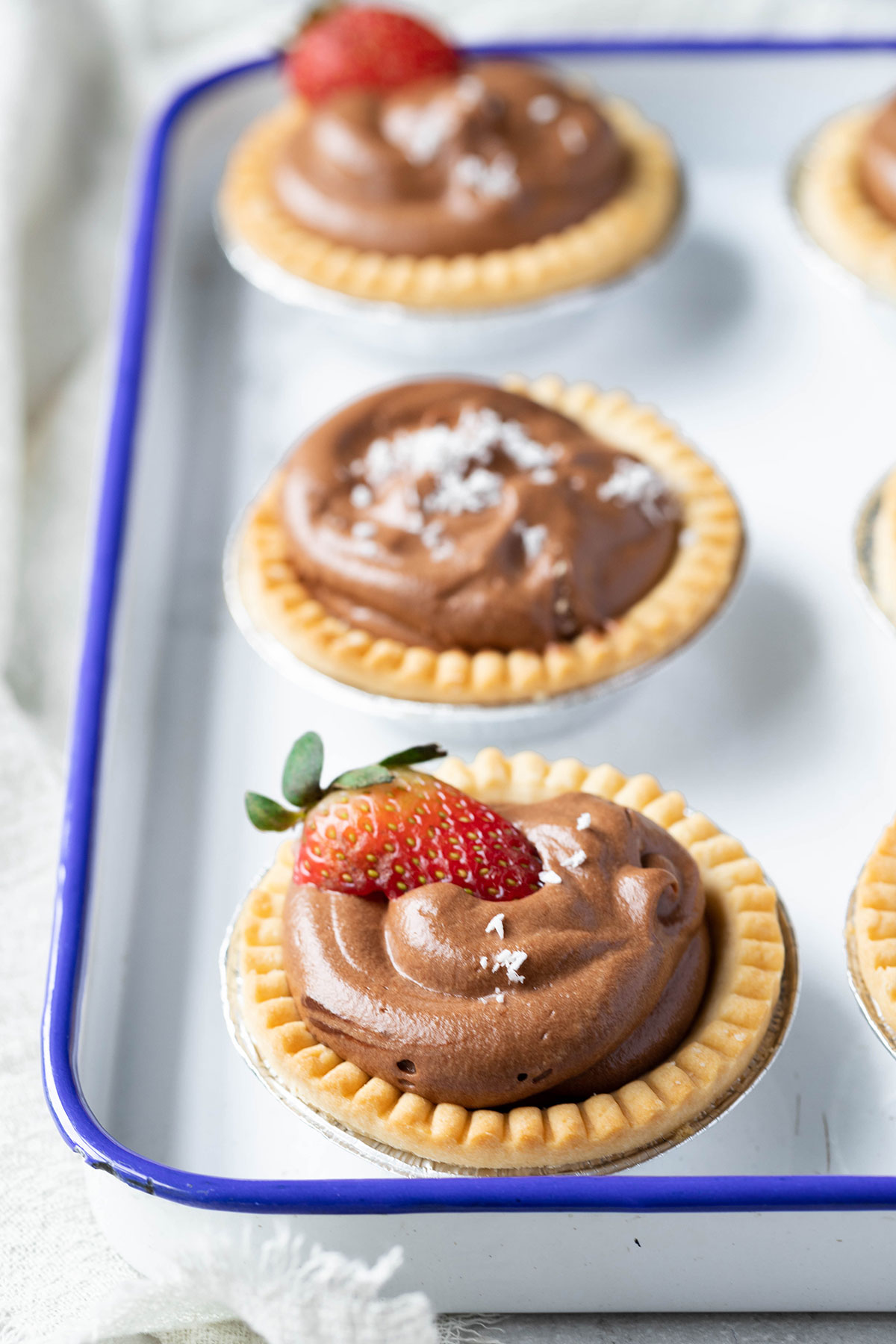 mini chocolate tarts in blue enamel tray topped with strawberries